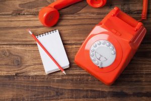 Red telephone on wooden table with notepad