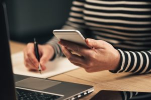 Woman writing contact list from phone into business agenda